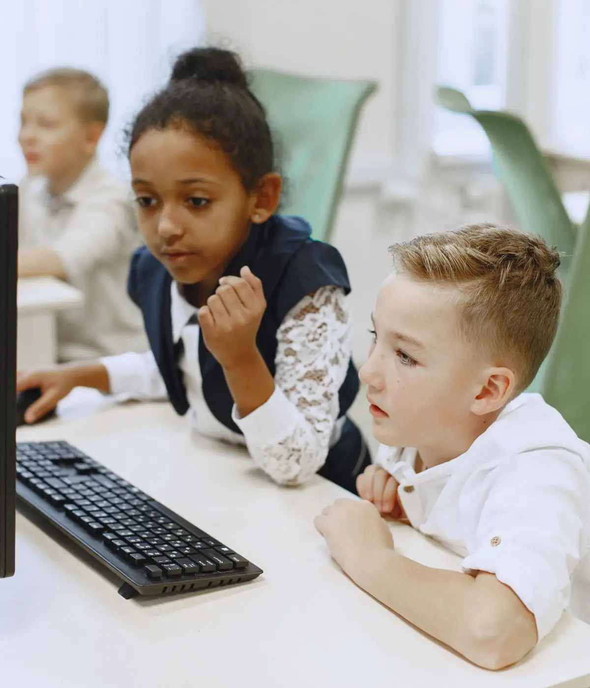 Tre bambini seguono con attenzione lo schermo di un computer in classe
